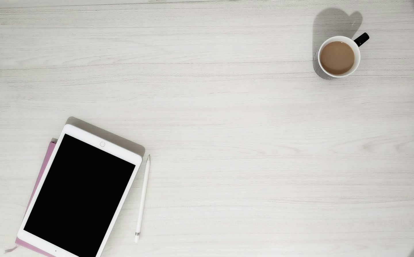 Tablet, stylus, notebook, and coffee mug on a wooden desk.